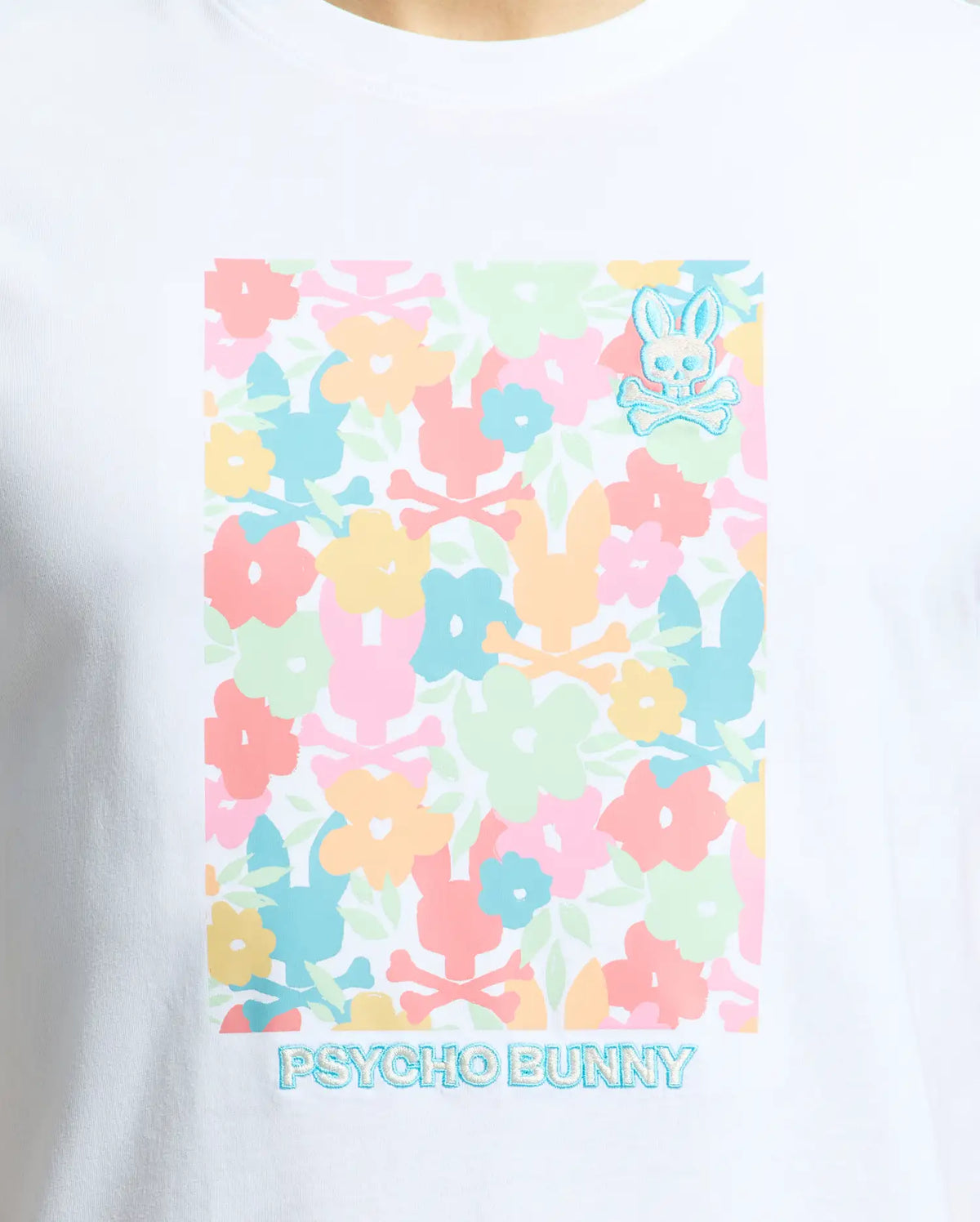 The Psycho Bunny Men's Lemmon Graphic Tee features a colorful floral design in pastel pink, blue, orange, and green on white Pima cotton. It includes the iconic Psycho Bunny logo and crossbones on the top right corner with "PSYCHO BUNNY" text across the bottom.