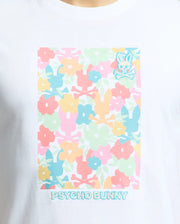 The Psycho Bunny Men's Lemmon Graphic Tee features a colorful floral design in pastel pink, blue, orange, and green on white Pima cotton. It includes the iconic Psycho Bunny logo and crossbones on the top right corner with "PSYCHO BUNNY" text across the bottom.