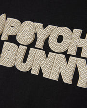 Close-up of the MENS MELVIN GRAPHIC TEE - B6U663C200 from Psycho Bunny, showcasing black fabric with "PSYCHO BUNNY" prominently displayed in large, textured, cream-colored letters. The distinctive HD-silicone print adds a three-dimensional effect to the text. Made from Pima cotton, this tee ensures both comfort and durability.