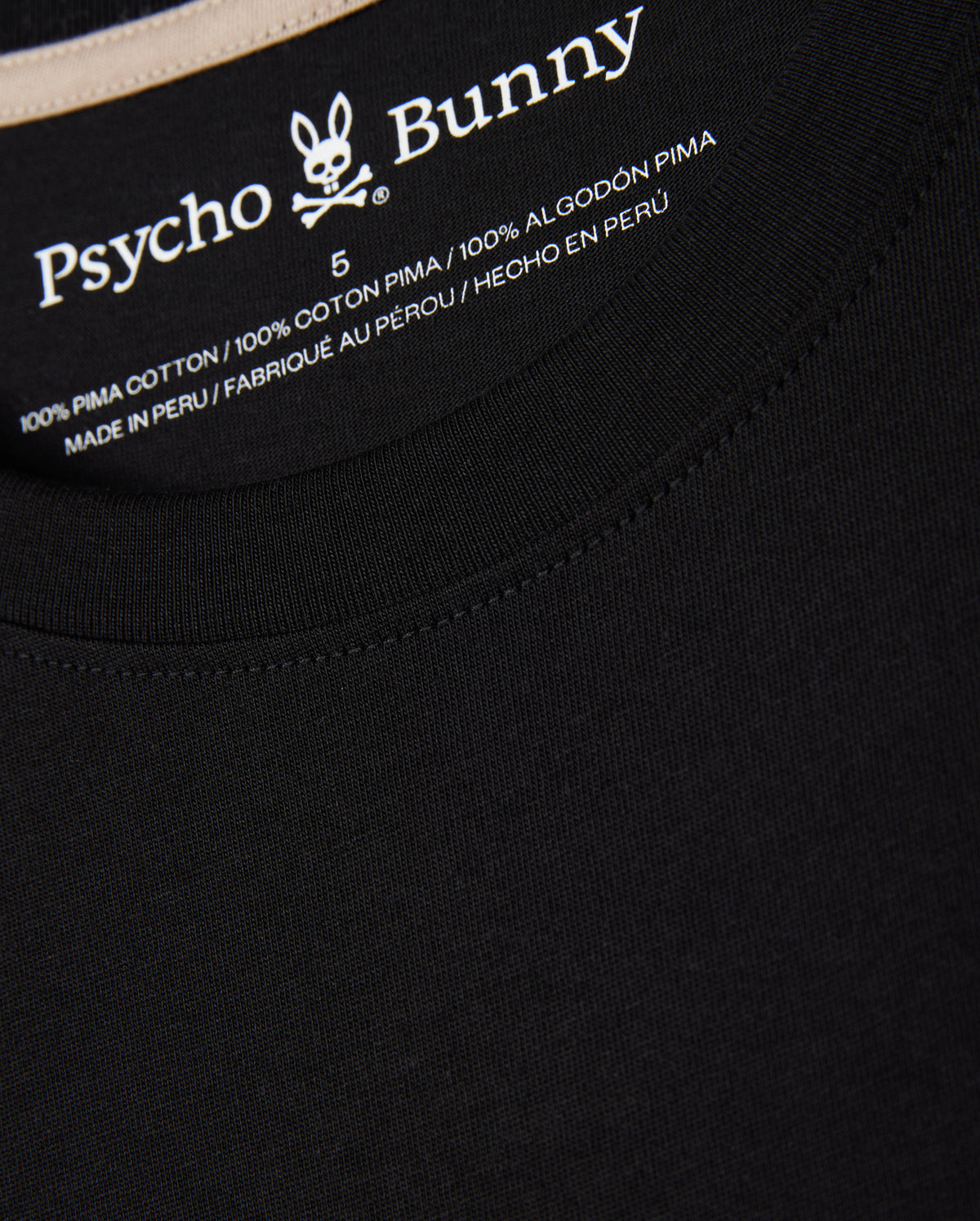 Close-up of the label inside the MENS MELVIN GRAPHIC TEE - B6U663C200 from Psycho Bunny. Made from 100% Peruvian Pima cotton and crafted in Peru, it ensures ultimate comfort in a regular fit. The Psycho Bunny logo, featuring a rabbit with crossbones, is visible above the text in an HD-silicone print.