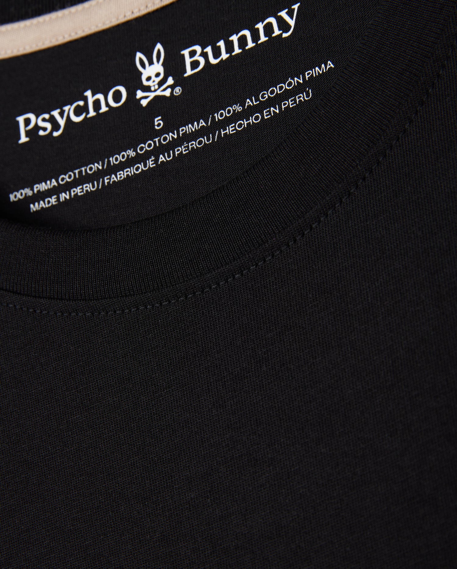 Close-up of the label inside the MENS MELVIN GRAPHIC TEE - B6U663C200 from Psycho Bunny. Made from 100% Peruvian Pima cotton and crafted in Peru, it ensures ultimate comfort in a regular fit. The Psycho Bunny logo, featuring a rabbit with crossbones, is visible above the text in an HD-silicone print.