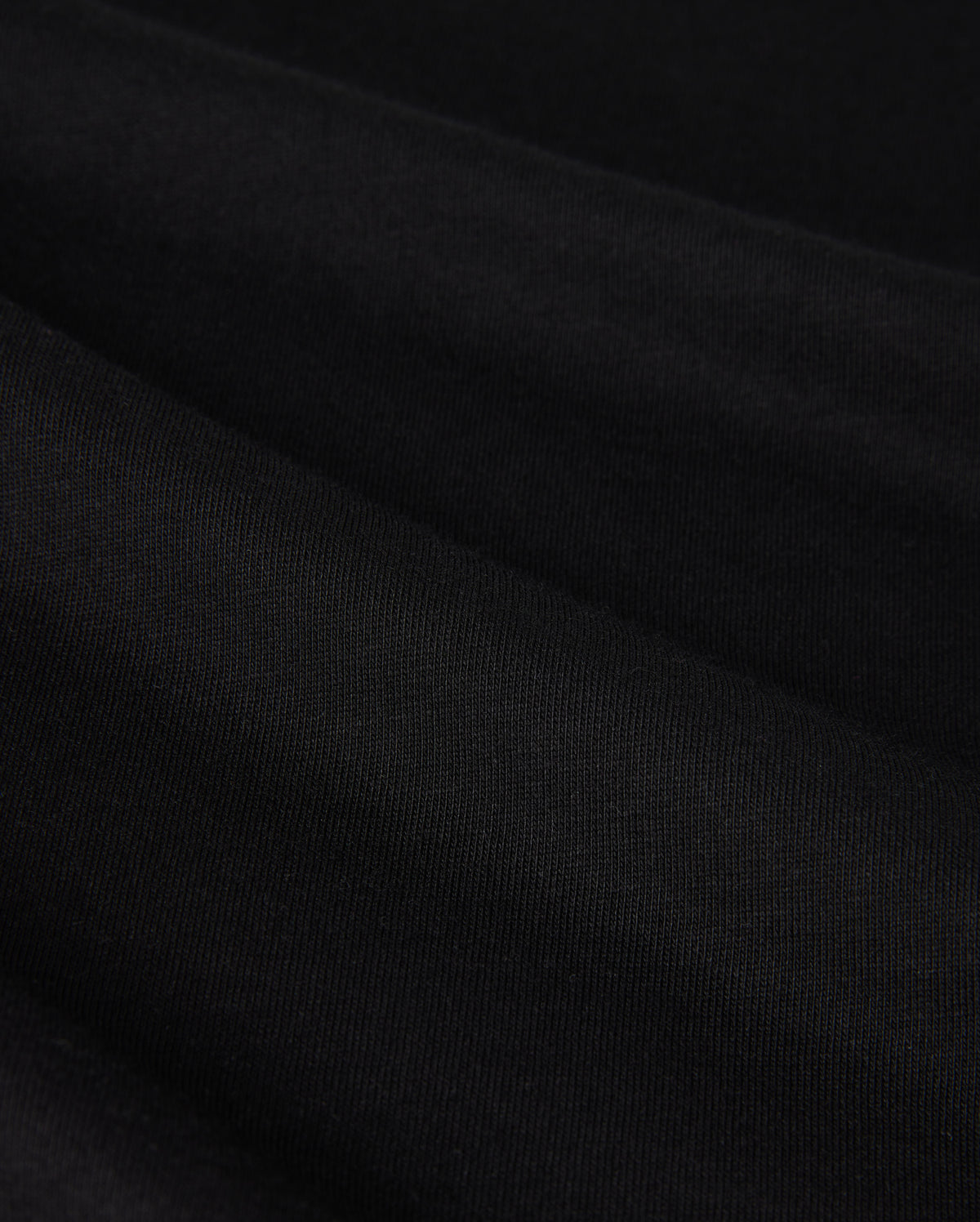 Close-up image of the MENS MELVIN GRAPHIC TEE - B6U663C200 by Psycho Bunny, showcasing its black fabric with a fine, smooth texture and subtle folds. The slightly reflective surface suggests a soft, possibly synthetic material. The image highlights the tee's uniformity and elegant draping, enhanced with an HD-silicone print for added detail.