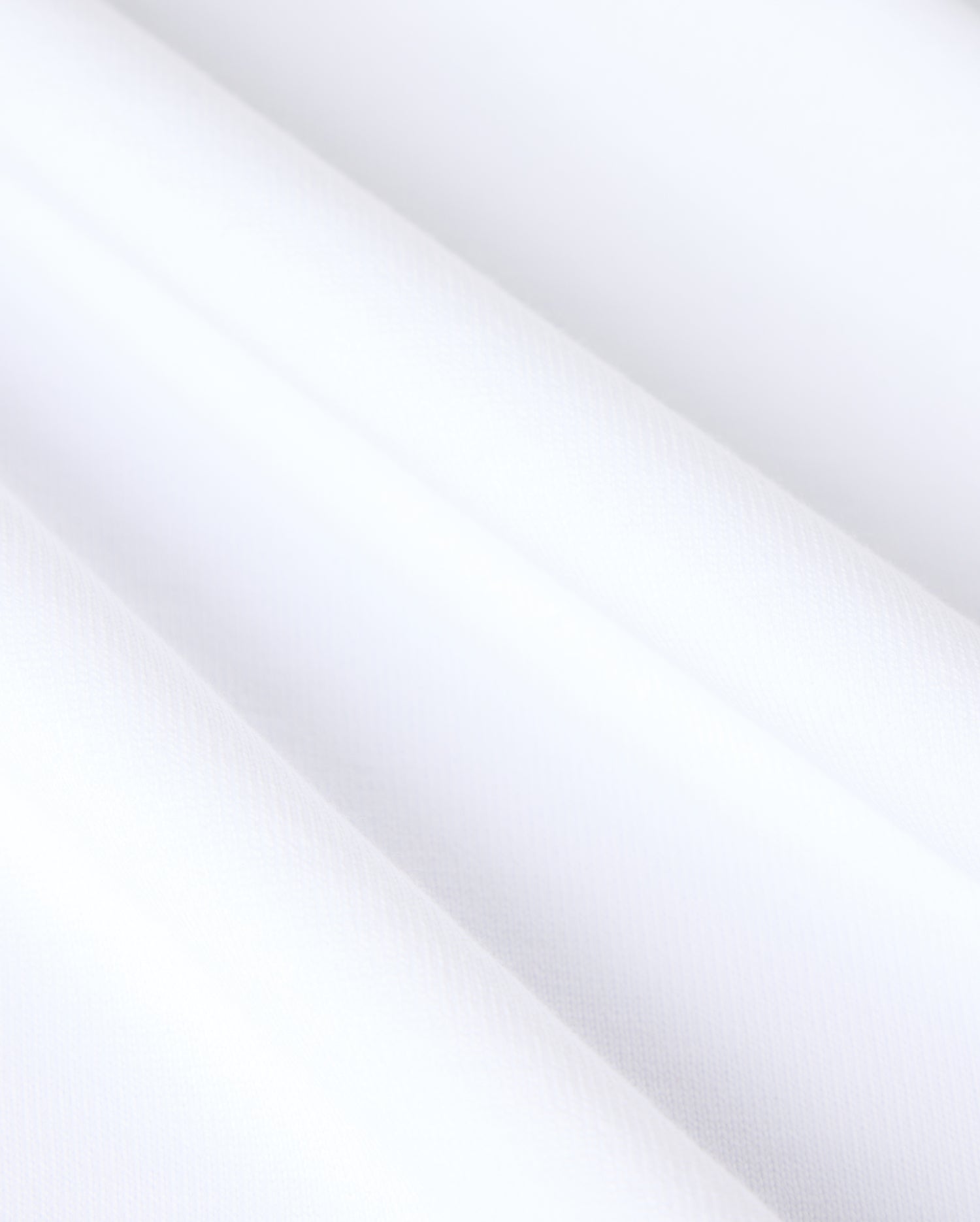 Close-up of heavyweight Pima cotton fabric on the MENS DUKE OVERSIZED TEE - B6U742D200 by Psycho Bunny, showcasing a smooth and clean surface. The solid pattern is evenly textured with subtle diagonal shadows, hinting at soft folds or gentle draping. The overall appearance is crisp, minimalistic, and bright.