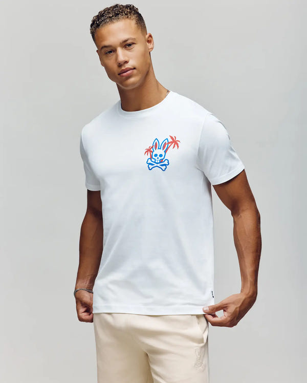 Wearing the Psycho Bunny MENS LOS ANGELES CITY TEE - B6U861A2PC, the individual sports a vibrant cartoon bunny and palm tree graphic on a white tee, paired with light pants. The look captures the relaxed Dodgers vibe against a neutral background.