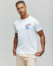 Wearing the Psycho Bunny MENS LOS ANGELES CITY TEE - B6U861A2PC, the individual sports a vibrant cartoon bunny and palm tree graphic on a white tee, paired with light pants. The look captures the relaxed Dodgers vibe against a neutral background.