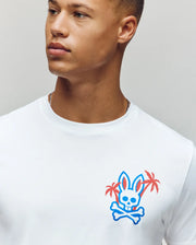 Sporting a Psycho Bunny MENS LOS ANGELES CITY TEE, a person flaunts a cartoon bunny head with crossbones and palm trees. The blue-outlined bunny with pink accents exudes a laid-back Dodgers vibe.