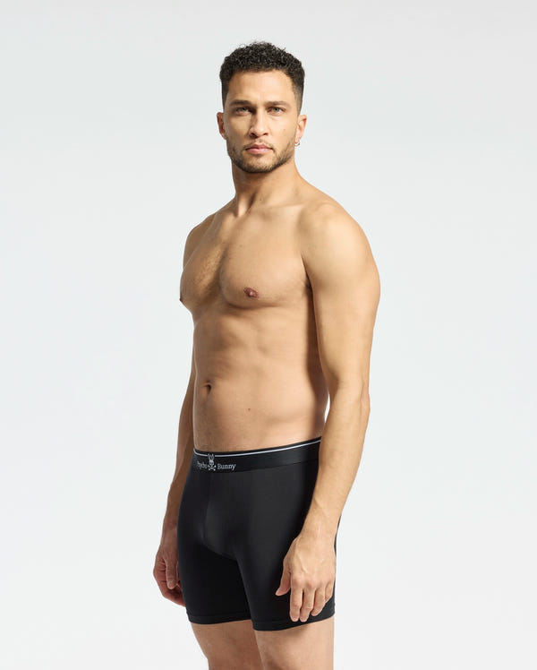 A man stands against a light gray background wearing the MENS SOLID KNIT 2 PACK BOXER BRIEF - B6V906ARCM by Psycho Bunny. He looks ahead with his arms at his sides, showcasing comfort and style in these ultrasoft modal-blend boxer briefs.