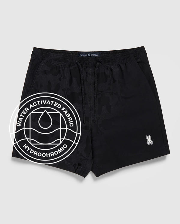 The Psycho Bunny MENS MALTA HYDROCHROMIC SWIM TRUNK (B6W321B2SW) features black camo bunny print, drawstring waist, left-leg logo, and “Water Activated Fabric” & “Hydrochromic” overlay with a water droplet icon.