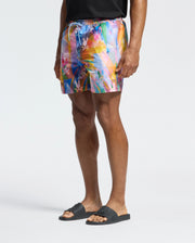 A person in a black t-shirt, Psycho Bunny's MENS MILOS PRINTED SWIM TRUNK - B6W446F200, and black sandals stands against a plain background, capturing a relaxed vacation vibe.