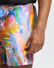 Dressed in Psycho Bunny's MENS MILOS PRINTED SWIM TRUNK - B6W446F200, this person showcases colorful shorts adorned with bunnies and skulls. Ideal for vacation, the quick-dry fabric promises comfort in and out of water.