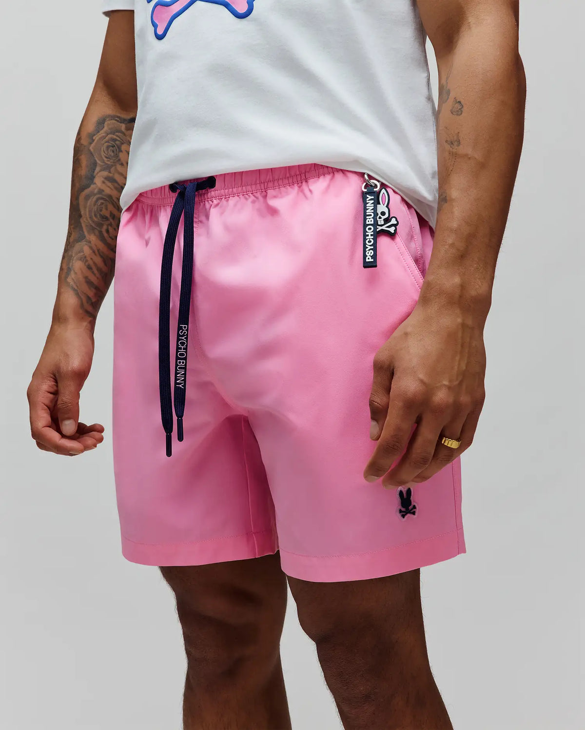 Mens Samos Hydrochromic Printed Swim Trunk, pink with a relaxed fit, smooth fabric, navy Psycho Bunny drawstrings, embroidered black bunny skull logo on left leg, and a Psycho Bunny keychain. (4)