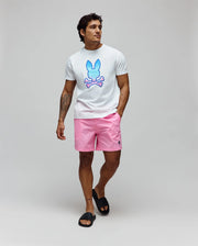 White jersey t-shirt with a large blue-to-pink gradient Psycho Bunny skull graphic on the chest, paired with Mens Samos Hydrochromic Printed Swim Trunk in pink, featuring a small dark embroidered bunny logo. (6)