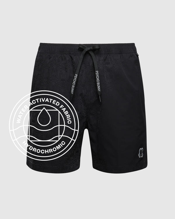 The Psycho Bunny MENS SAMOS HYDROCHROMIC PRINTED SWIM TRUNK features a drawstring waist, subtle hydrochromic pattern, and small logo at the hem. A circular "Water Activated Fabric Hydrochromic" overlay with droplet icon appears on the left.