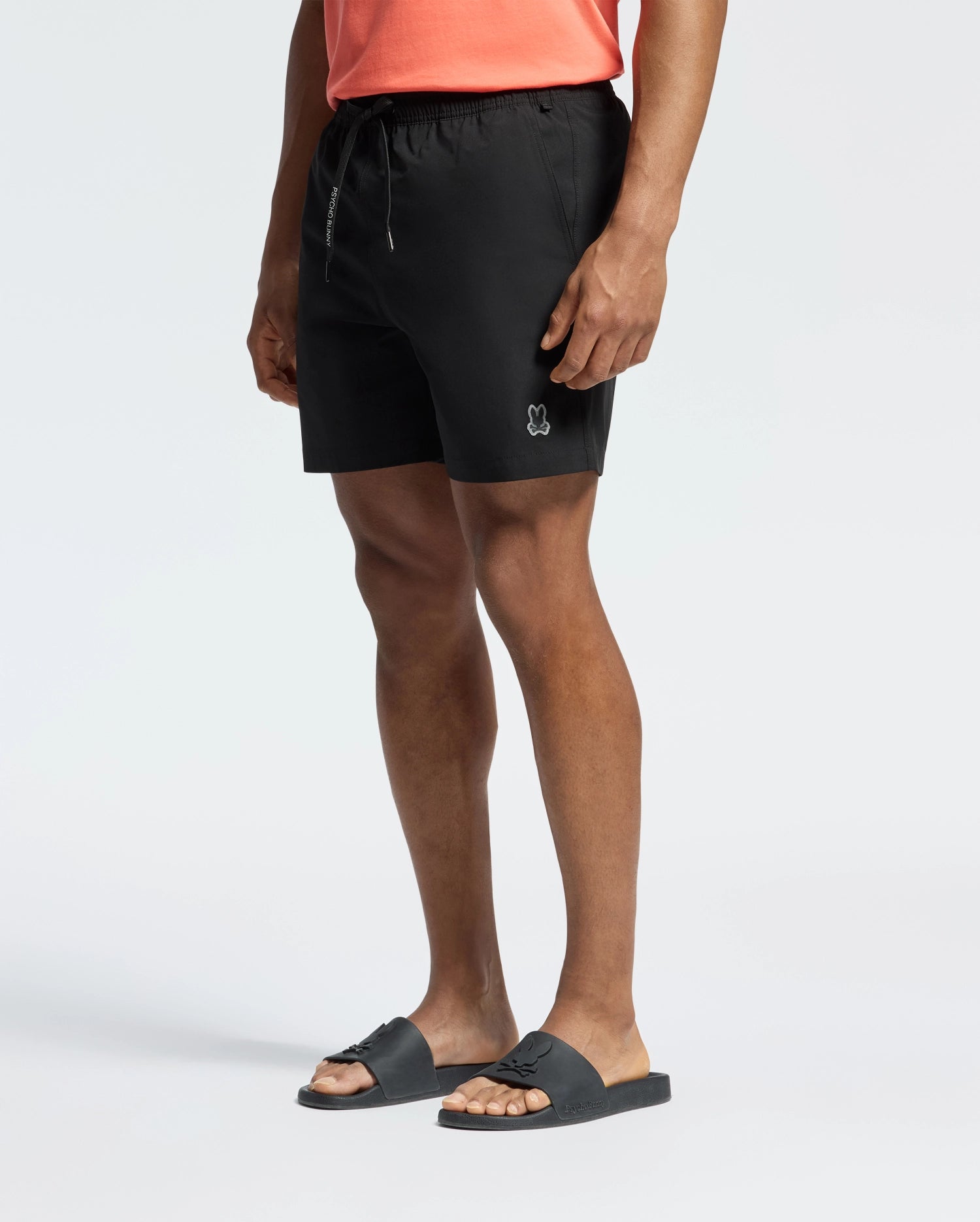 Black Mens Samos Hydrochromic Printed Swim Trunk, classic fit, smooth quick-dry fabric, with an elastic drawstring waist featuring white Psycho Bunny text and a small embroidered grey skull logo on the left thigh.