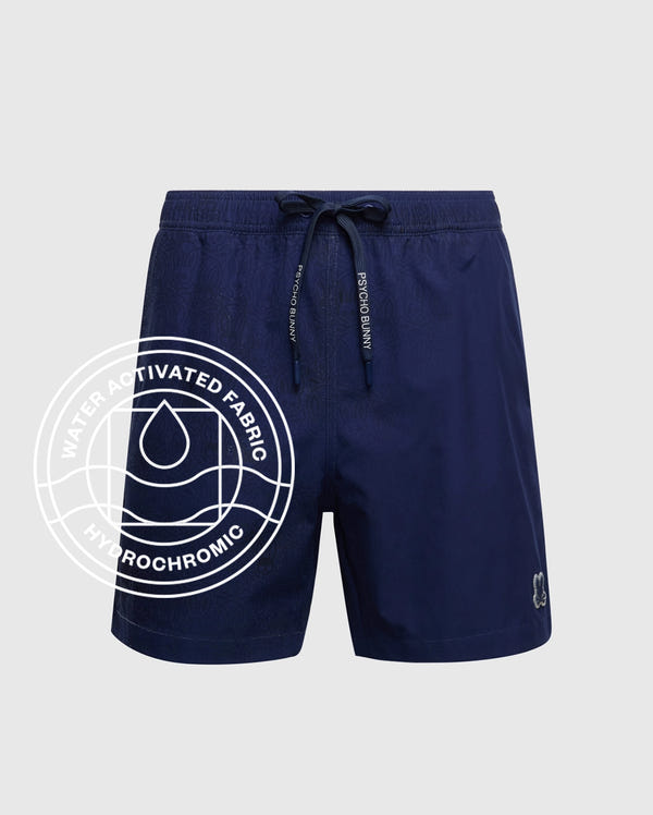 The Psycho Bunny MENS SAMOS HYDROCHROMIC PRINTED SWIM TRUNK (B6W453F200) in navy features a drawstring waist, subtle branding, and hydrochromic “water activated fabric” with a water droplet icon on the left leg.