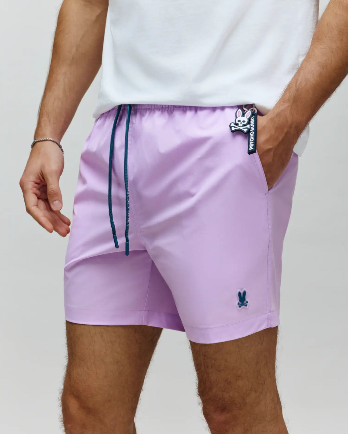 Mens Samos Hydrochromic Printed Swim Trunk in lavender, featuring dark teal drawstrings, a small embroidered Psycho Bunny logo on the left leg, and a larger Psycho Bunny keychain.
