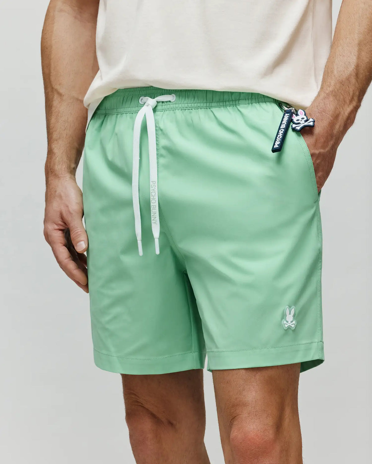 Mens Samos Hydrochromic Printed Swim Trunk in mint green, relaxed, with white Psycho Bunny drawstrings, a small white bunny skull logo on the left leg, and a Psycho Bunny keychain.