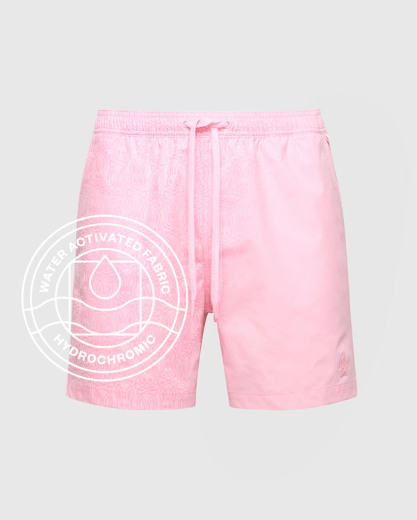 The Psycho Bunny MENS SAMOS HYDROCHROMIC PRINTED SWIM TRUNK (B6W453F200) features pink swim shorts with a subtle bunny pattern, drawstring waist, and a “Water Activated Fabric Hydrochromic” label for innovative style. Displayed on a light background.
