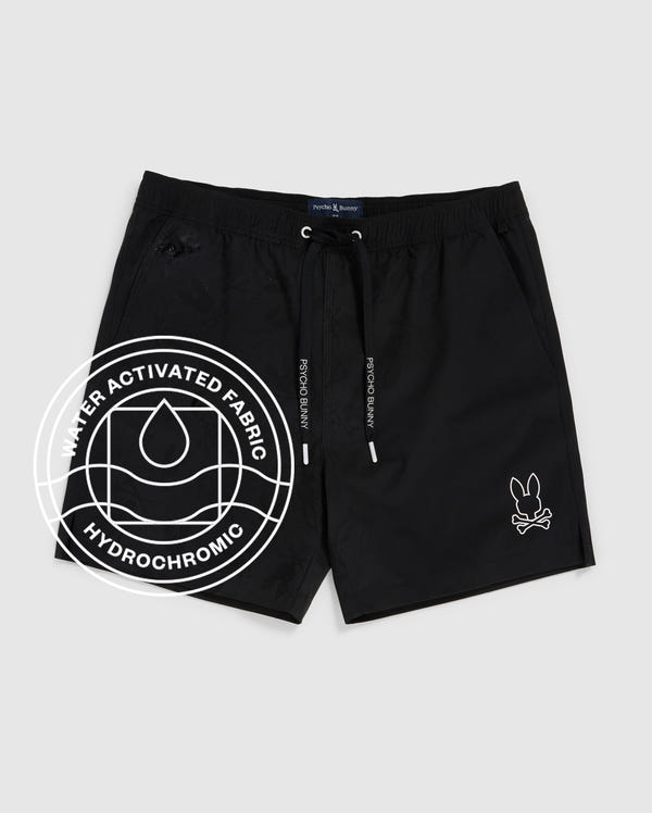 The Psycho Bunny MENS PARKER HYDROCHROMIC SWIM TRUNK (B6W646C200) features a black hydrochromic fabric, white bunny skull logo on the left leg, black drawstrings, and a "Water Activated Fabric Hydrochromic" label on the side.