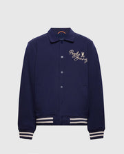 The navy MENS BIG AND TALL DESERT COACH BOMBER JACKET - B9J428F200 by Psycho Bunny is crafted from a comfortable cotton blend and features a button-up front with ribbed cuffs and hem. It boasts white "Psycho Bunny" embroidery and a bunny logo on the left chest, merging classic charm with modern flair.