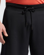 A person wearing Psycho Bunny MENS BIG AND TALL LEVANZO FRENCH TERRY SWEATSHORT - B9R578F200 in black, with only their lower torso and left hand visible against a plain background.
