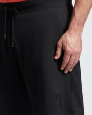 A close-up of a person wearing Psycho Bunny MENS BIG AND TALL LEVANZO FRENCH TERRY SWEATSHORTS (B9R578F200) with a drawstring waist and embroidered bunny logo, their right hand resting by their side.