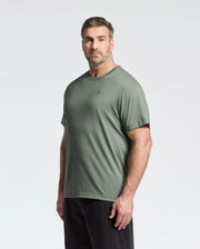 A bearded man with short hair wears a green Psycho Bunny B9U014CRPC Pima cotton crew neck tee featuring a small chest logo and black pants. He stands against a light background, facing slightly left with a neutral expression.