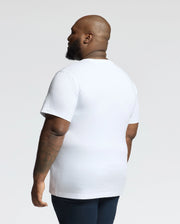 A person with a shaved head wears Psycho Bunny's MENS BIG AND TALL CLASSIC CREW NECK TEE - B9U014CRPC in white, paired with dark pants. They turn slightly to the side, looking away against a plain white background. This Pima cotton tee is essential for any men's wardrobe.