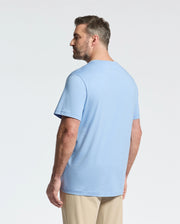 A bearded man with short hair stands slightly to the right, wearing a Psycho Bunny BIG AND TALL CLASSIC CREW NECK TEE (B9U014Z1PC) in light blue, made of 100% Pima cotton, paired with beige pants. The background is plain white.