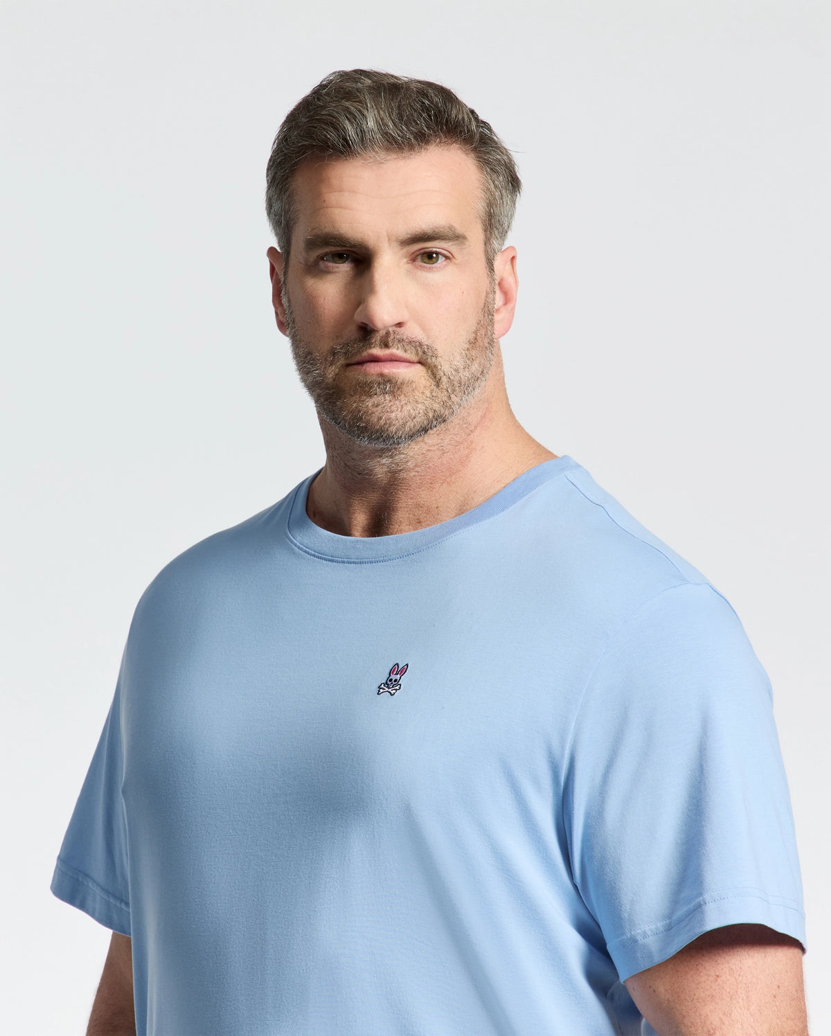 A man with short, light brown hair and a beard wears a light blue Psycho Bunny Big and Tall Classic Crew Neck Tee (B9U014Z1PC), 100% Pima cotton, featuring a small logo on the chest against a plain, light-colored background.