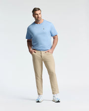 Wearing a Psycho Bunny BIG AND TALL CLASSIC CREW NECK TEE in light blue and beige pants, a man stands confidently with hands in pockets against a white background. He sports white sneakers, short hair, and a beard, showcasing effortless style.