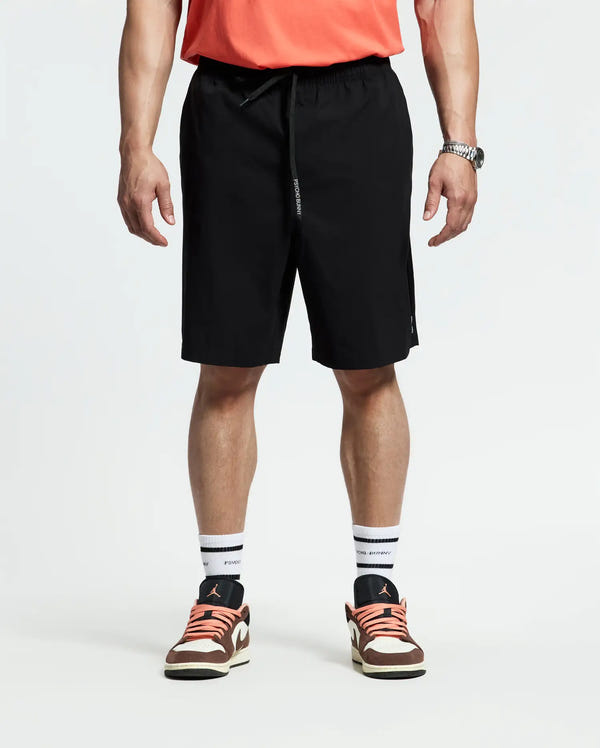 A person wears a coral t-shirt, white socks, black, white, and coral sneakers, and Psycho Bunny MENS BIG AND TALL SAMOS HYDROCHROMIC SWIM TRUNK (B9W453F200), standing against a plain white background with relaxed hands by their sides.