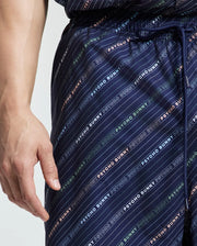 A person is wearing Psycho Bunny's blue MENS BIG AND TALL RENMARK PB PRINTED SWIM TRUNK with a quick-dry logo-patterned print. Their relaxed left hand rests by their side, while the drawstring peeks at the waist, ideal for laid-back beach days.