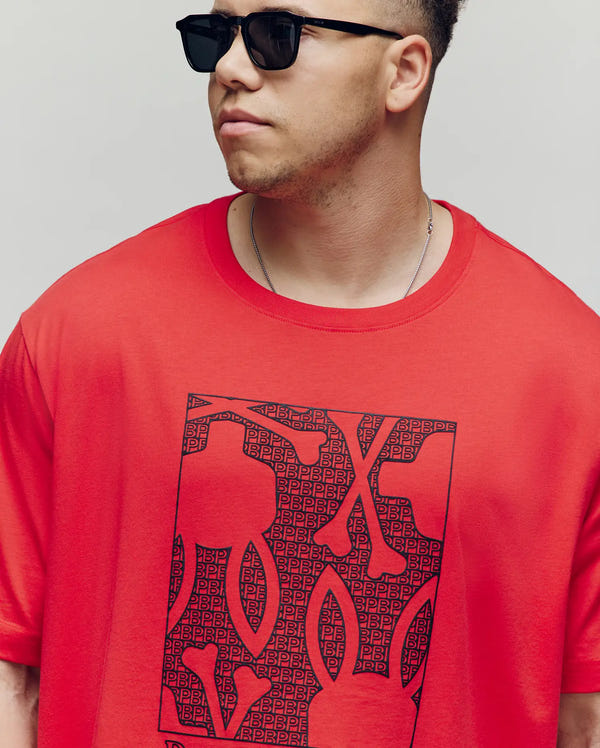 A man in black sunglasses and a Psycho Bunny MENS BIG AND TALL GLENN GRAPHIC TEE (BT0200006), made from 100% Pima cotton with a bold black water-based print, stands against a plain light background looking to the side.