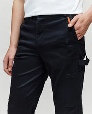 A person wears black Psycho Bunny KIDS RUSSELL CARPENTER PANT (KB0600001) with cargo pockets and a small embroidered bunny logo, paired with a partially visible white shirt; one hand in a pocket, the other by their side.