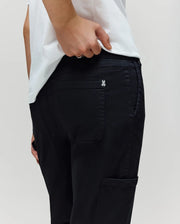 A person in a white shirt and Psycho Bunny KIDS RUSSELL CARPENTER PANT (KB0600001) stands with one hand on the waistband near the back pocket, showing a small silver butterfly emblem on the pocket.