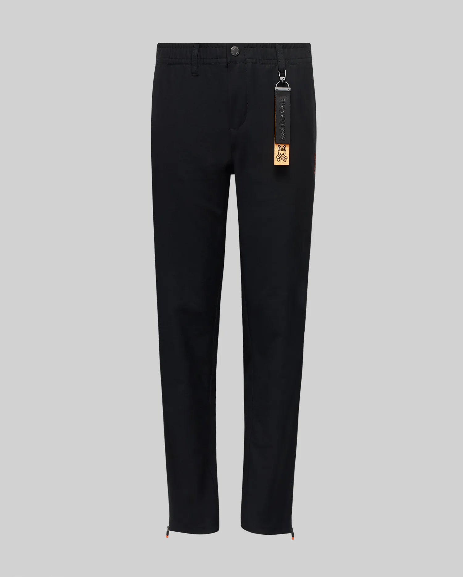 The Psycho Bunny KIDS MATHIEU COMMUTER PANT (KB0600002) features a black, straight-leg classic fit with a button and zip fly, elastic waistband, and a black tag with brown accent on the belt loop. Minimalist design shown on gray background.