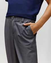 A person wearing a navy blue shirt and Psycho Bunny KIDS MATHIEU COMMUTER PANT - KB0600002 in classic fit gray, featuring bunny embroidery on the pocket, stands with their right hand in the pocket. Only torso and upper legs are shown.