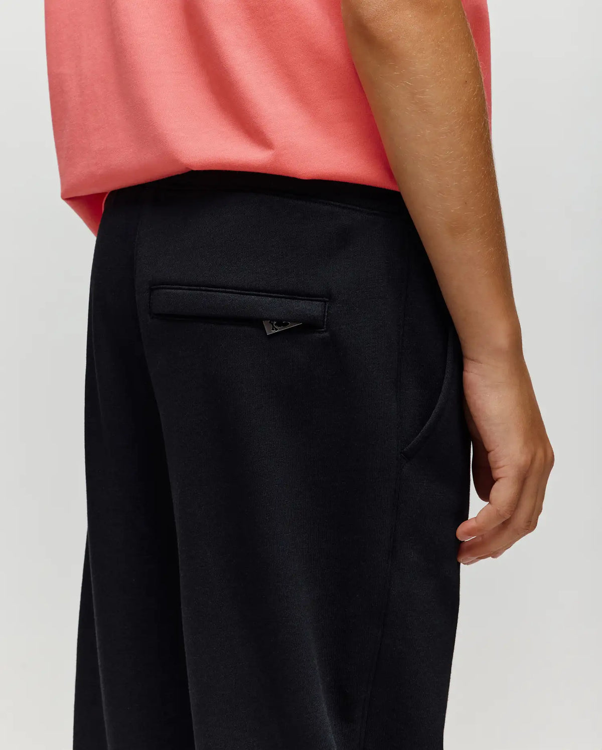 A person in Psycho Bunny KIDS WADE SWEATPANT - KB0800002 stands with their right arm relaxed, highlighting the back pocket and side seam details that showcase its classic athletic style.