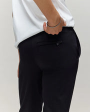 A person in Psycho Bunny’s KIDS WADE SWEATPANT (KB0800002) slips a hand into the zippered back pocket, showing off classic athletic style and premium cotton-blend comfort with a touch of effortless flair.