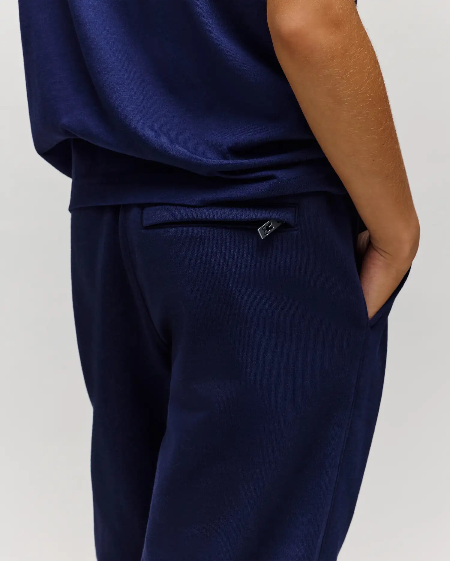 A child models the Psycho Bunny KIDS AUGUSTE JOGGER - KB0800003 in dark blue with a matching 100% cotton top, one hand in their pocket, shown from the side and back against a plain light background.