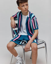 Kids Cliff Knit Short and matching collared shirt in a relaxed fit, featuring bold teal, pink, white, and navy vertical stripes with a ribbed knit texture and small embroidered Psycho Bunny skull logo on the left chest. (3)