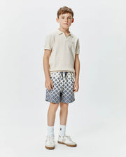 Classic fit cream pique knit polo with embroidered Psycho Bunny logo on chest, paired with Kids Tobias Swim Trunk featuring a white base and intricate blue geometric pattern, drawstring waist. (4)