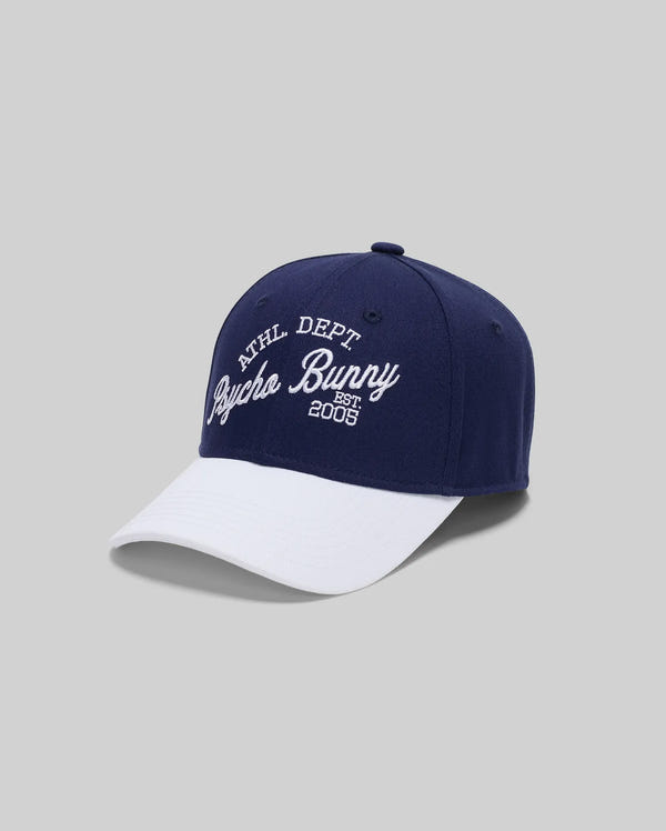 The Psycho Bunny KIDS MATTEO BASEBALL CAP (KO1500002) is a varsity-style navy cotton twill cap with a white curved brim, featuring "ATHL DEPT Psycho Bunny EST. 2005" embroidered on a light gray front background.