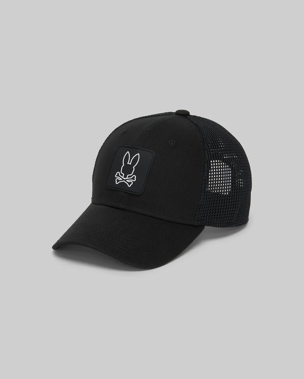 The Psycho Bunny KIDS DARIO TRUCKER CAP (KO1500009) is a stylish black cap with a breathable mesh back, adjustable snap-back, and features a white bunny head above crossed bones patch on the front. Shown on a plain grey background.