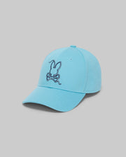 The KIDS CYRUS BASEBALL CAP (KO1500014) by Psycho Bunny features a light blue cotton twill design with a dark blue bunny and crossbones embroidery on the front, shown against a plain gray background.