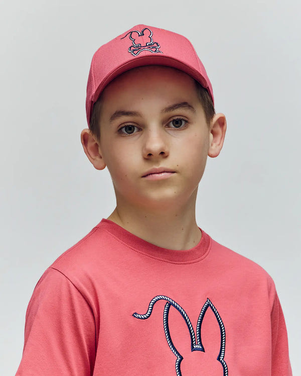 A boy in the Psycho Bunny KIDS CYRUS BASEBALL CAP (KO1500014) and a matching pink tee with bunny ears and embroidered logo looks directly at the camera against a plain light background.