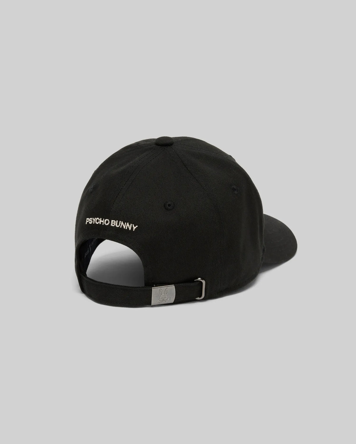 The KIDS WADE BASEBALL CAP - KO1500016 by Psycho Bunny is a black cotton twill cap shown from the back with "PSYCHO BUNNY" text, a white embroidered Bunny on the left, and an adjustable metal buckle strap against a plain light gray background.