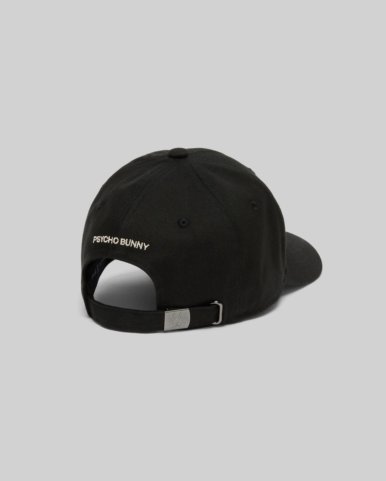 The KIDS WADE BASEBALL CAP - KO1500016 by Psycho Bunny is a black cotton twill cap shown from the back with "PSYCHO BUNNY" text, a white embroidered Bunny on the left, and an adjustable metal buckle strap against a plain light gray background.