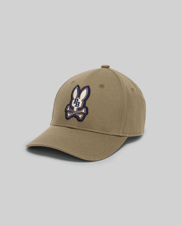 The KIDS WADE BASEBALL CAP (KO1500016) by Psycho Bunny is a khaki cotton twill cap with six panels, a curved brim, and an embroidered Bunny patch showing a cartoon bunny head above crossed bones with "PB" initials.